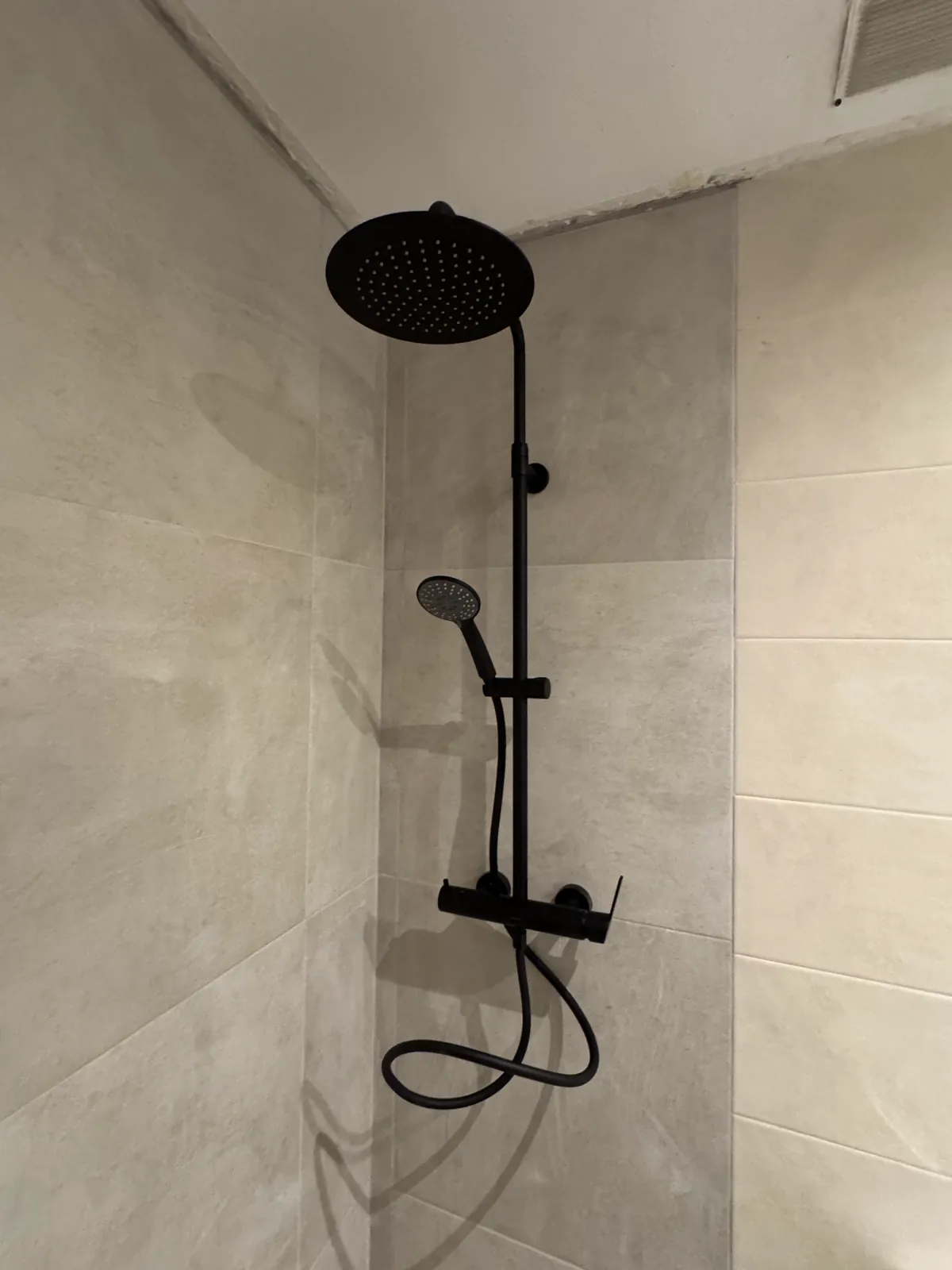 Ducha con grifería negra instalada en un baño reformado